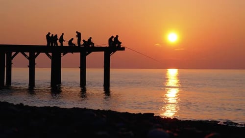 Silhouetten von Fischern mit Angelruten bei Sonnenuntergang auf dem Pier. Zeitlupe.