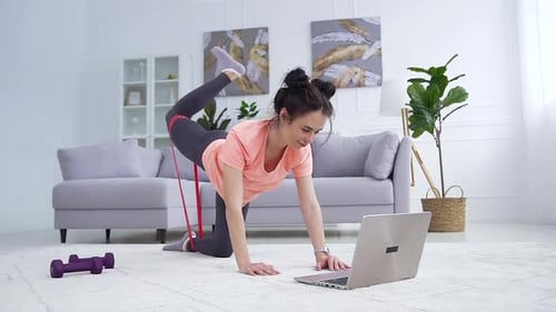 Fille en tenue de sport faisant du fitness avec une sangle d'étirement pendant l'examen de l'entraînement sportif sur ordinateur portable