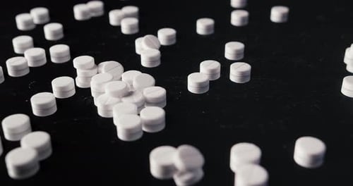 Pills Falling onto Dark Surface