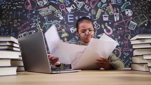 Serious little Asian girl checking homework and studying online on laptop in working room at home