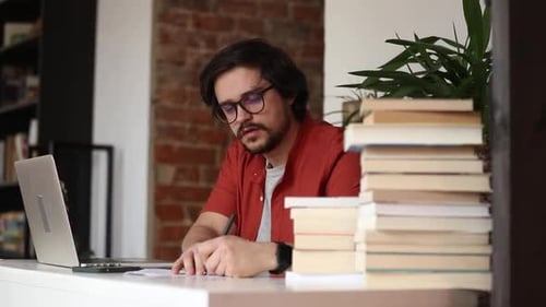 Stylish man sitting at table in home office and using laptop