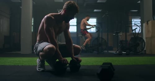 a Male Bodybuilder After a Circular Cardio Workout Sits on the Floor of the Gym and Rest Gaining