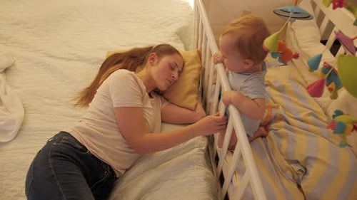 Mother Sleeping as Baby Smiles in Crib