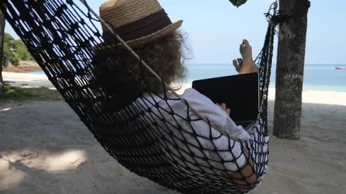 Geschäftsfrau arbeitet mit Laptop in Hängematte am Strand