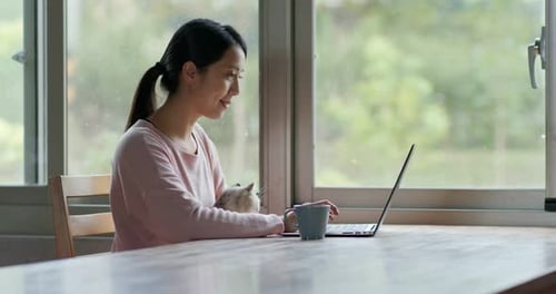 Frau arbeitet mit ihrer Katze zu Hause am Laptop