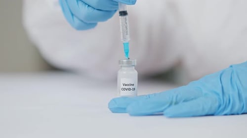 Closeup of Doctor Hands in Blue Gloves Injecting Needle in Covid19 Vaccine Ampoule and Pumping