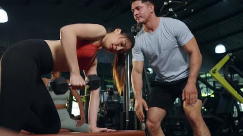 4K Asian woman do weight training workout lifting dumbbell with male sport trainer at gym.