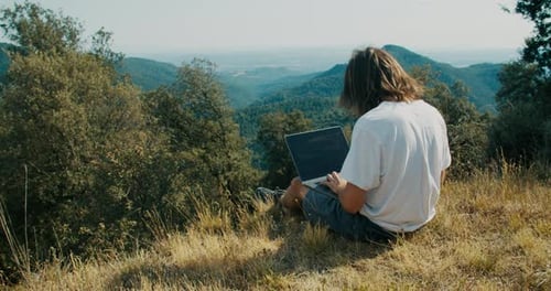 Man Working Remote on Summer Journey with Notebook Computer Sit on Mountain