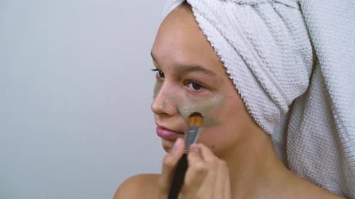 Adolescente ayant des problèmes de peau appliquant un masque facial à l'argile au spa à domicile