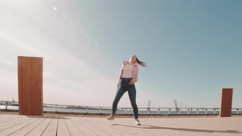 Young Woman Dances on a Wood Deck Under Blue Sky