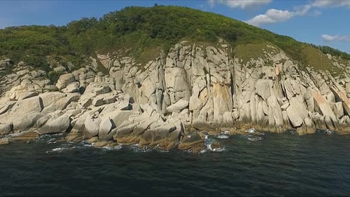 Luftaufnahme, die sich an einem sonnigen Tag entlang der Küste des tiefblauen Meeres entlang einer Dramatisch Klippe bewegt