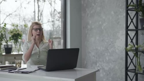 Freudige Unternehmerin mit Brille für Vision genießt Geschäftserfolg beim Sitzen am Tisch