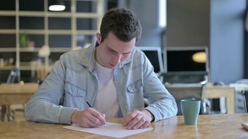 Young Designer Thinking and Writing on Paper in Modern Office