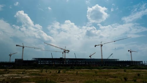 Las grúas torre que trabajan en un sitio de construcción levantan una carga en un edificio alto al anochecer. Un gran contras