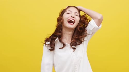 Woman Twirling Her Hair and Laughing on Yellow Background
