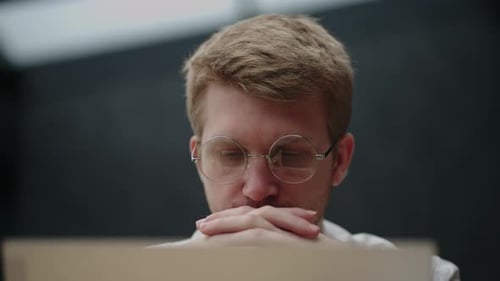 Thoughtful Young Adult in Glasses Looks Down