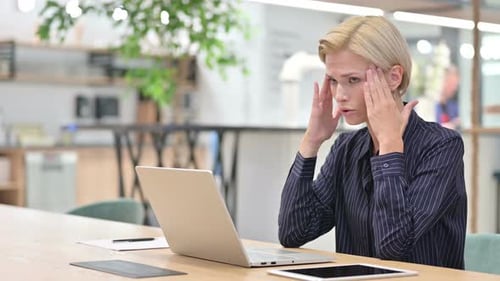 Stressed Businesswoman with Laptop Having Headache in Office