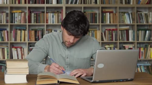 Étudiant masculin utilisant un ordinateur portable étudiant à la bibliothèque universitaire