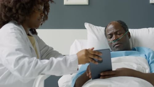 Doctor Explaining Tablet to Patient in Hospital Bed