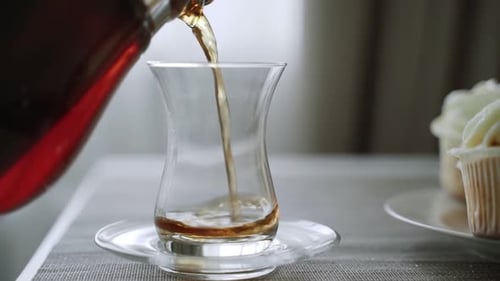 Schwarzer Tee wird aus der Teekanne in eine große transparente Glasschale gegossen