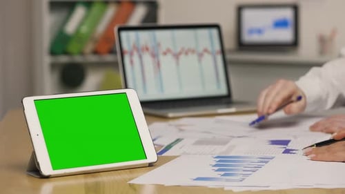 Man and Woman Viewing Papers with Charts and Graphs Using Laptop