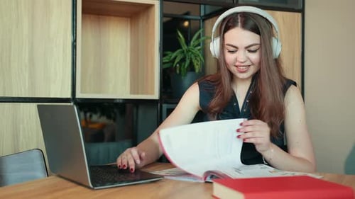 Woman Works on Laptop with Headphones and Book
