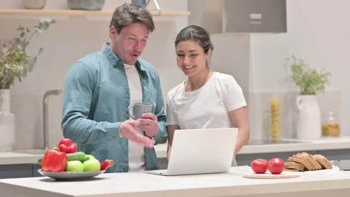 Smiling Couple Uses Laptop in Bright Kitchen