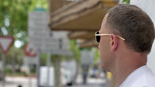 Young attractive man in sunglasses stands on the street and watches