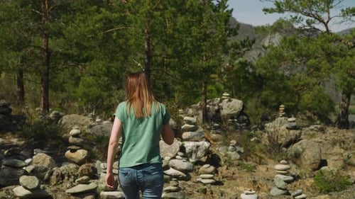 Woman Walks Between Symbolic Old Stone Piles Near Fir Forest