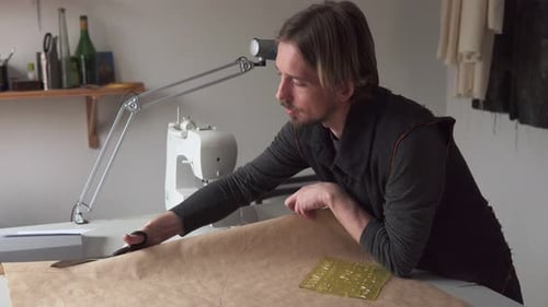Man Tailor with Scissors Making Clothing Pattern While Working in Workshop