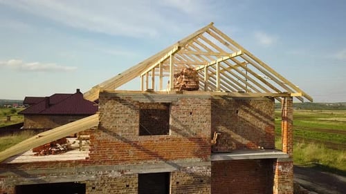 Aerial view of unfinished brick house with wooden roof frame structure under construction.