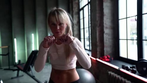 Porträt einer schlagenden Frau während des Boxtrainings im Fitnessstudio, sie schlägt mit den Händen zur Kamera