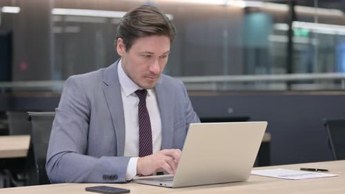 Businessman in Suit Typing on Laptop in Office