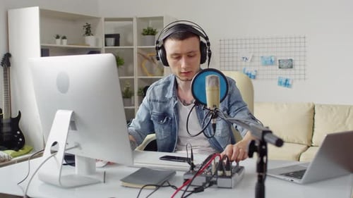 Man Adjusting Audio Mixer at Computer Workstation