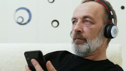 Senior Man Listening on Headphones, Holding Phone