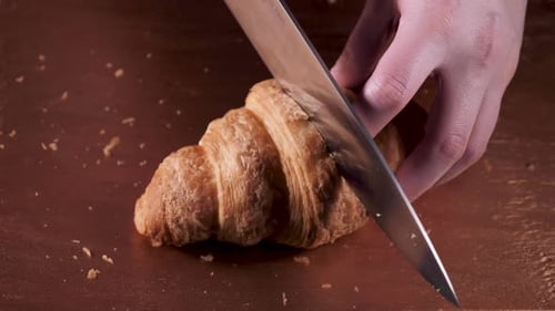 Hands Slice Crispy Croissant on Bronze Cutting Board