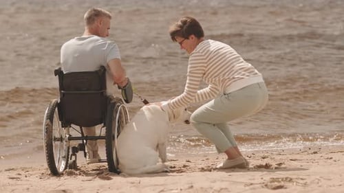 Man in Wheelchair with Wife and Their Dog on Beach