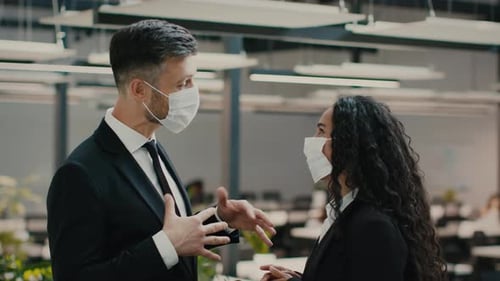Businessman And Businesswoman In Face Masks Talking Standing In Office