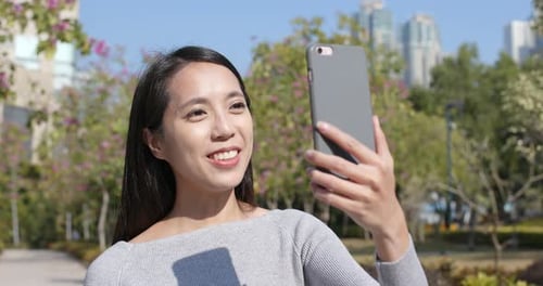 Woman Records Video on Phone in Sunny City Park