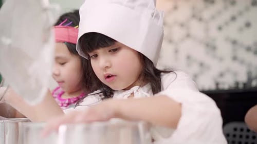 Gruppe von Kindern, die gemeinsam Kuchen im Klassenzimmer backen, multiethnische Jungen und Mädchen machen glücklich beim Backen.