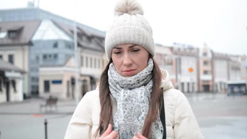 Woman Adjusts Hat and Scarf in Urban Setting
