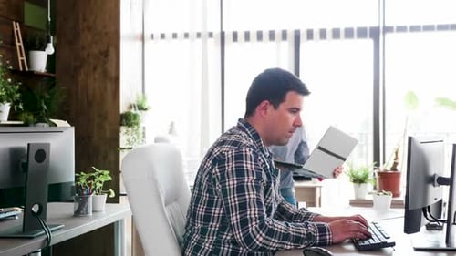 Jeune homme d'affaires dévoué travaillant sur son ordinateur pendant que ses gestionnaires viennent à son bureau