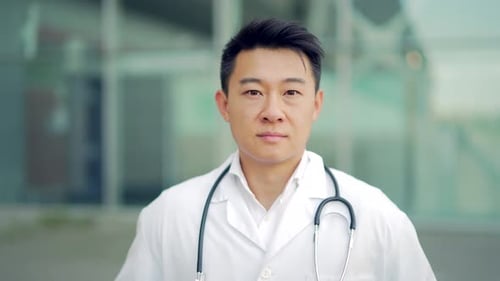 Close up portrait of Asian doctor looking at camera with arms crossed on background