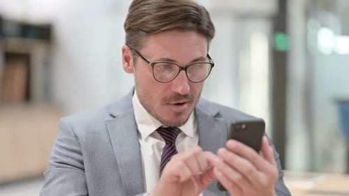 Man Cheers While Looking at Smartphone in Office
