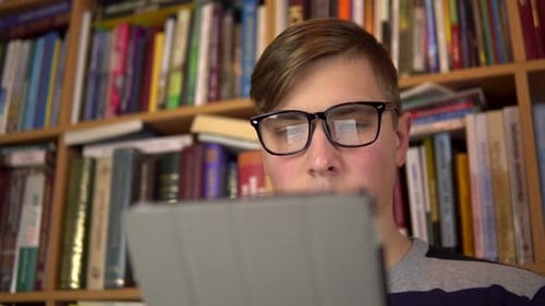 Student Reads Tablet in Front of Bookshelf
