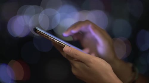 Hands Using Smartphone at Night with Bokeh Lights