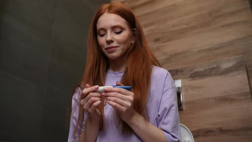 Young Woman Looks at Pregnancy Test in Bathroom