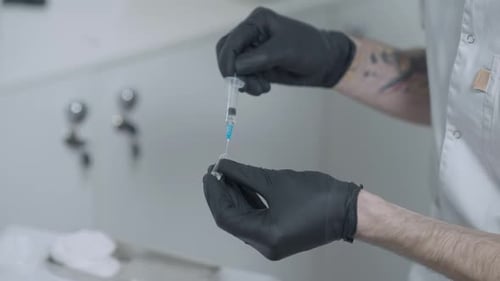Closeup Unrecognizable Tattooed Male Beauty Therapist Filling Syringe with Anesthetic or Botox