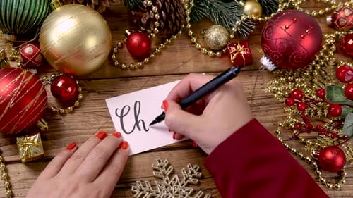 Woman Writes Christmas on Greeting Card With Decorations