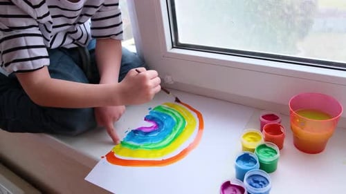 Child Paints Colorful Rainbow Picture on Windowsill